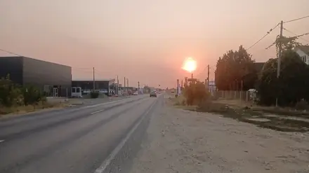 The DN65 in the last kilometres before Craiova, looking west into the sun — single carriageway, hard shoulders, showrooms and dealers strung along the road