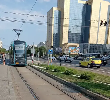 A blue low-floor tram on line 101 to Ford standing at an island stop on Calea București, Craiova, the gold glass tower behind it