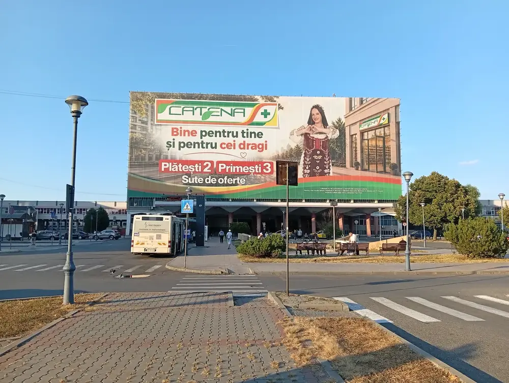 The station from the square, buses and taxis under the canopy — the whole front wrapped in an advertising banner in August 2026