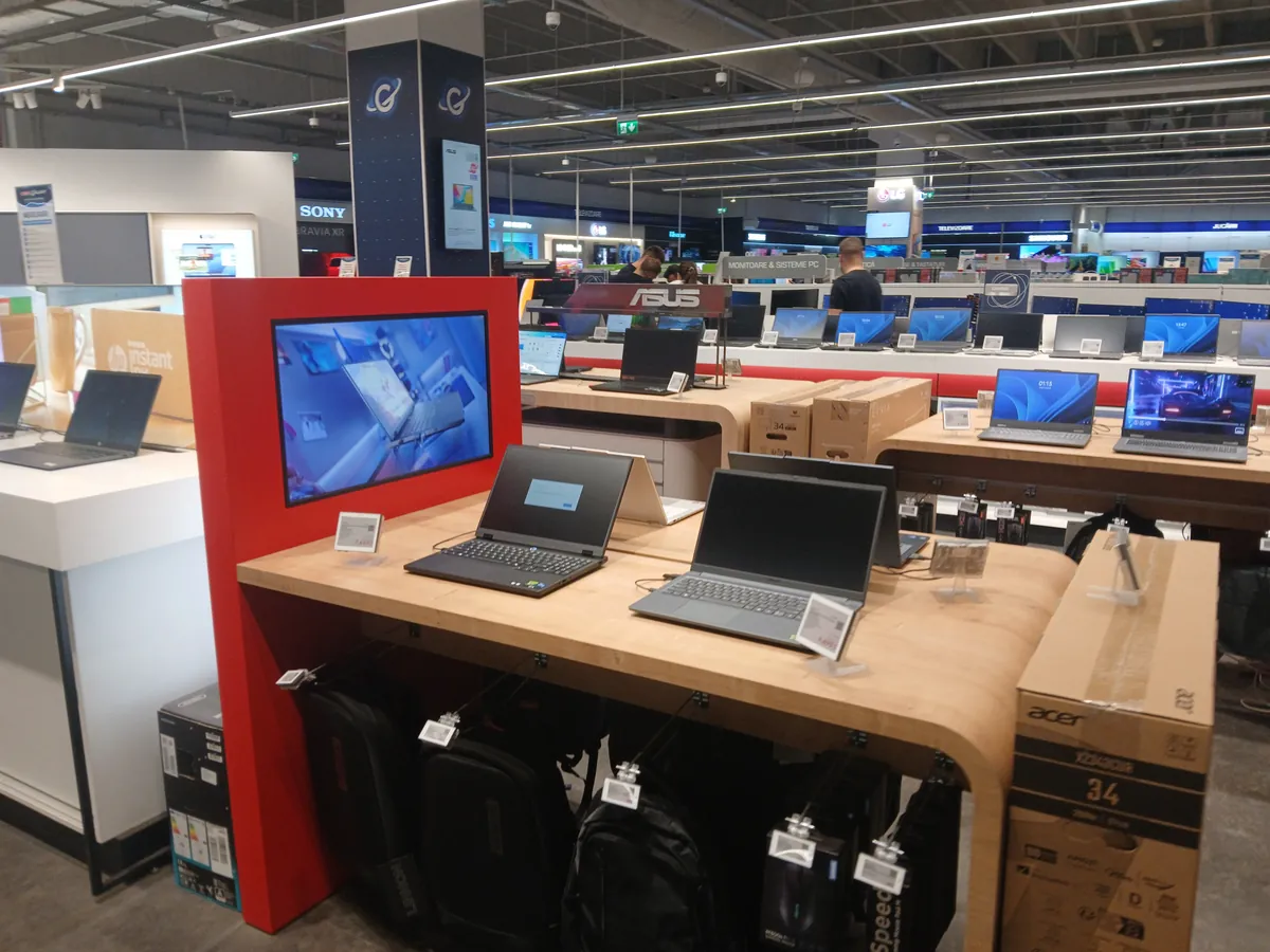 Laptop tables inside Media Galaxy Craiova with rows of laptops on display, Asus and Sony stands and the monitors and PC systems aisle behind, September 2026