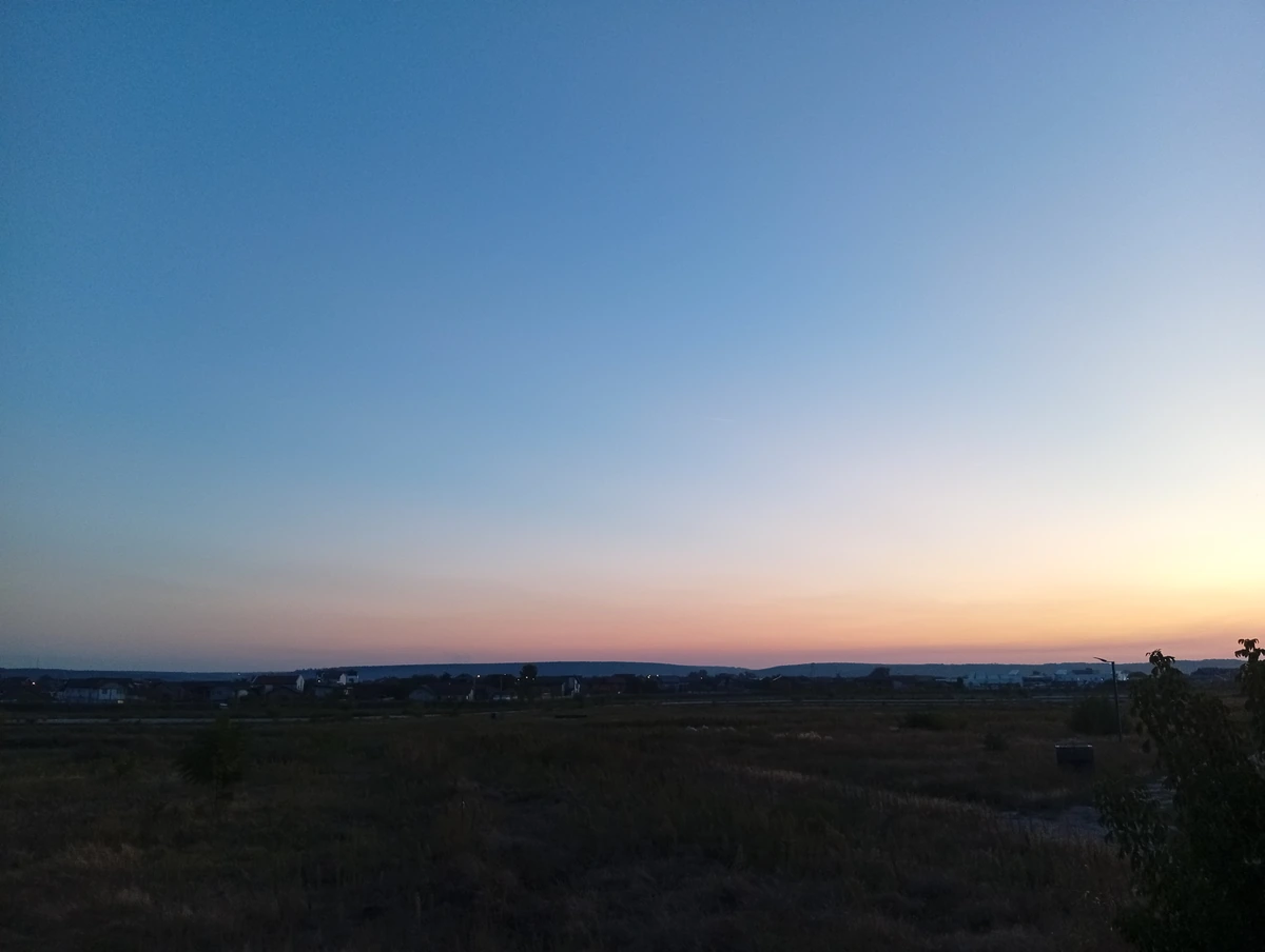 Dusk panorama on the edge of Craiova: empty grassland, rows of houses and low hills under a blue-to-orange sky, 20 September 2026