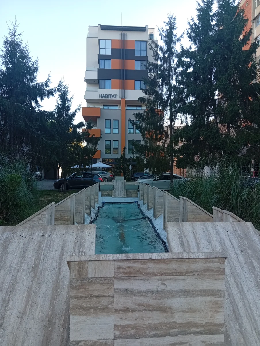 Looking down the channel from the pavement end at dusk, the Habitat block framed between the spruces. September 2026