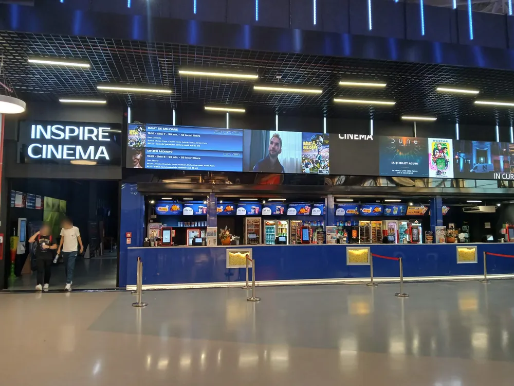 Inspire Cinema on the upper level, October 2026: the box office and snack bar under a wall of screens showing the evening’s films