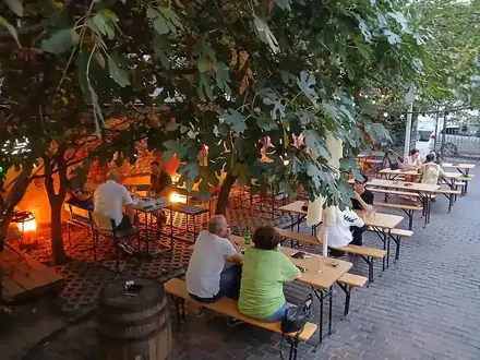 Old Court Biergarten in Craiova — trestle benches under a fig tree, festoon lights and wine barrels in a walled yard at dusk