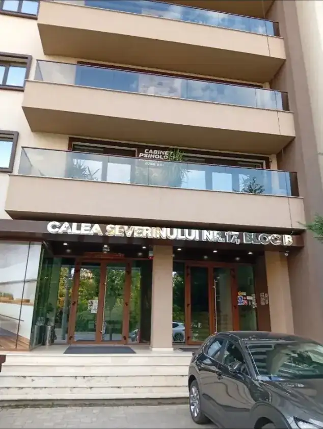 What a newer block looks like at the door: glass balconies, a lit lobby, the address in brass over the entrance and a psychologist’s practice on the first floor — flats in these are the ones that come with a lift and a working intercom