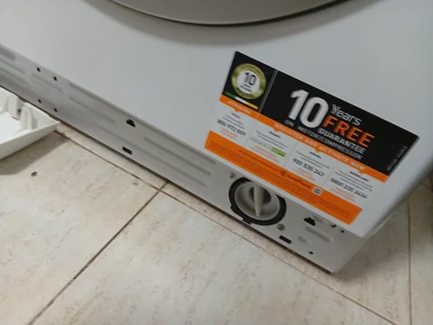 The bottom front of the washer with the strip removed, the filter cap at the lower right and the strip lying on the tiles